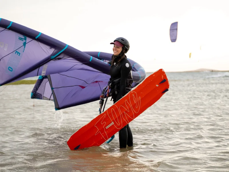 Kitesurfeuse avec son aile violette et sa planche orange dans l’eau