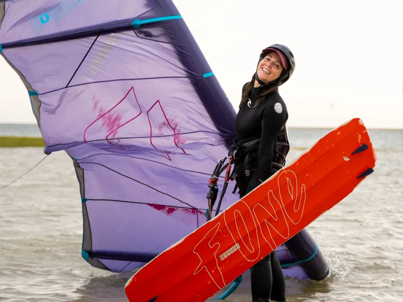 Kitesurfeuse avec son aile violette et sa planche orange dans l’eau